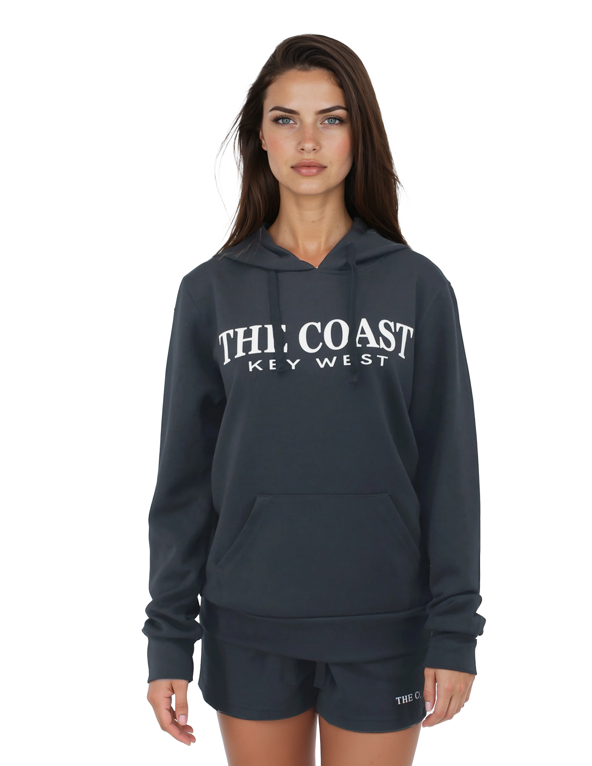 A woman modeling a dark charcoal gray hoodie with 'THE COAST KEY WEST' printed in white across the chest, paired with matching shorts, against a plain white background.