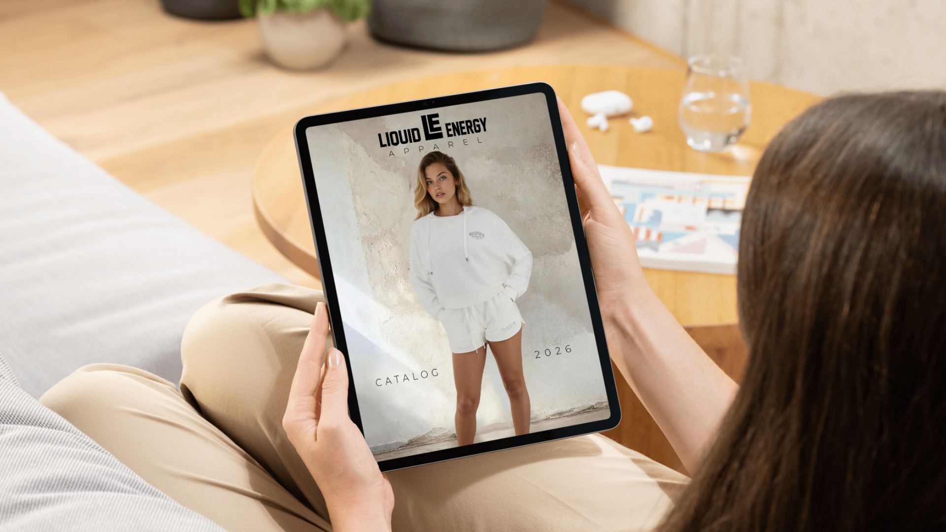 Person holding a tablet with a Liquid Energy catalog on a wooden table.