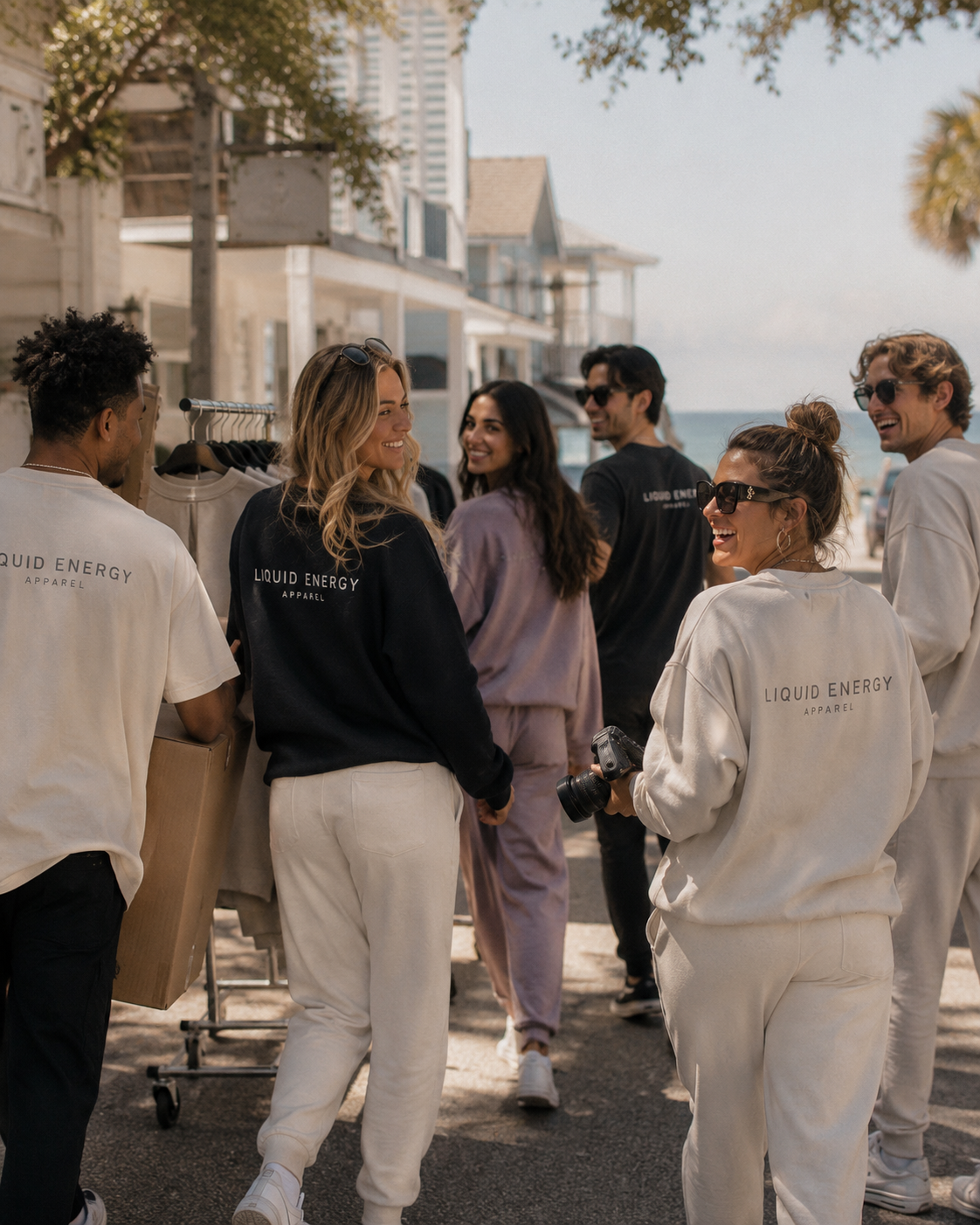 A group of people wearing matching Liquid Energy Apparel tracksuits and sweatshirts, standing outdoors on a street with buildings and trees in the background.